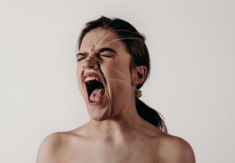 Woman screaming with eyes closed, with thin threads stretched across her face, symbolising emotional captivity and psychological distress.
